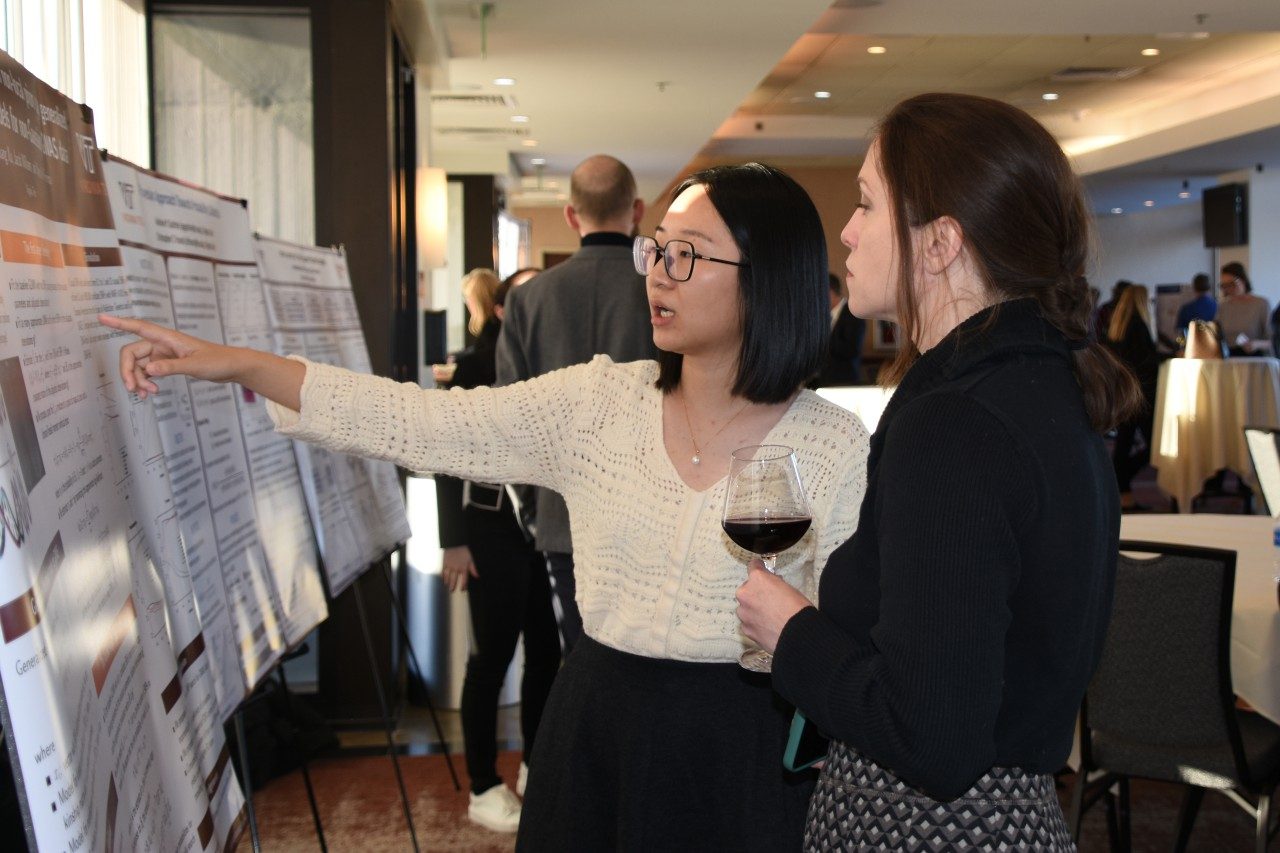 Student points to her project poster during a conversation with an event attendee.